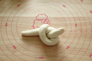 然后如图，像打结一样，长条右半部分顺时针绕在左半部分上方，然后将右半部分的尾部从圆孔中取出。类似打结手法。