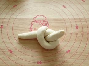 然后如图，像打结一样，长条右半部分顺时针绕在左半部分上方，然后将右半部分的尾部从圆孔中取出。类似打结手法。