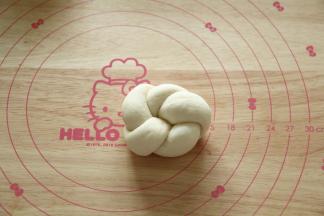 然后将右边的长条尾部往面团底下压，左边的长条尾部从上方塞入之前的圆孔中，将左右两头的尾部捏紧即可。略微整理，就是5瓣花型，如果搓的长条够长，可以制作成6瓣花型。