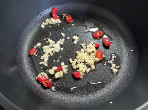 接着来烧酱汁。锅中倒入少量油，大概20-30ml玉米油，下蒜末和小米椒，煸炒至蒜香味出来。然后加小半碗水。