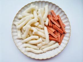 首先准备好所有食材。香肠撕开包装，对半切开，再对半切，再切成和年糕差不多的长条。