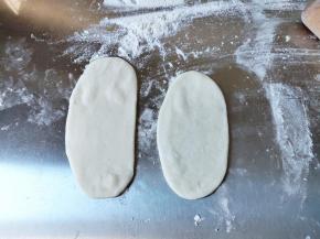 用擀面杖从中间分别往上往下擀薄，不要来回擀，如果有空气，不要擀破，不然后面鼓不起来。案饼上最好洒一点面粉或淀粉，不然饼胚不好拿起来。