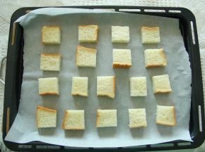 5、吐司块放在垫了油纸的烤盘上。尽量排均匀一些！此时可以预热烤箱，上下150度预热一会。