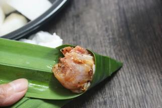 5.取一片香兰叶像包粽子一样先对折出一个圆锥形，放入腌制好的鸡腿肉块，包好后用牙签固定，放蒸盘中