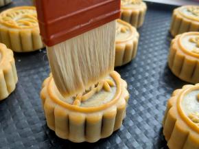 第一次烤制后，月饼花纹定型，室温放置不烫手后，用羊毛刷沾少许的蛋黄液，速度给表面刷一层蛋黄水，侧面不要刷，一定要控制蛋黄水不要流到侧面，尽量做到只有表面一层，全部完成后再入180度预热好的烤箱10-12分钟，这个时间根据自己烤箱调整。