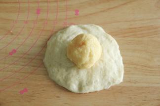 步骤14、取一个松弛好的面团，按扁，擀开成中间厚，两边薄的圆形面片，翻面，放上馅料球。