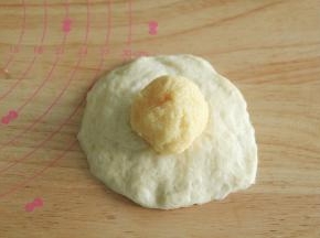 步骤14、取一个松弛好的面团，按扁，擀开成中间厚，两边薄的圆形面片，翻面，放上馅料球。