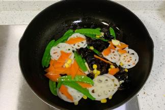 倒入胡萝卜、玉米、黑木耳、藕片和荷兰豆翻炒片刻。