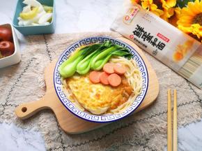 将面条盛入碗里，放上煎蛋，摆上小青菜和火腿肠片，浇上汤汁。