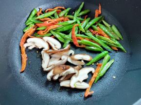 着下四季豆、香菇和辣椒煸炒一下，炒至变色也盛起。四季豆一定要炒熟。（前面如果焯过水，这一点稍微煸炒几下就成。）