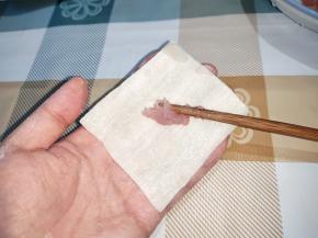左手托住一块面皮，右手用筷子从盘子里拨出一团肉馅放面皮中间，肉馅比花生米大一点。