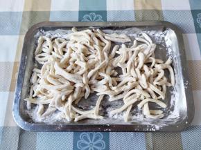 肉丝和配菜准备好了，面团也醒得差不多了。我们来剪面条了。如果动作快的，可以直接对着锅剪。我一般都是先剪好再煮的。准备一个大托盘，洒一些玉米淀粉或干面粉防粘。将面团捏扁，用剪刀剪成一条条的。面条大概四五毫米左右粗，剪得粗一些的可以拉扯一下，扯细一点。剪得多了，也要撒一层玉米淀粉，不然粘一团就成面疙瘩了。