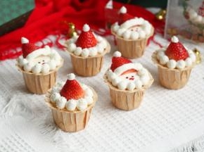 步骤12、草莓在中间的纸杯，沿着草莓周围挤一圈奶油球，草莓顶部也要挤一个，然后撒上一些椰蓉，雪花飘落的感觉。草莓在头部的纸杯，同样先围着挤一圈奶油球，顶部挤上一个，沿着草莓底部挤上圣诞帽围边，然后用黑色素调淡奶油或者直接黑巧克力融化，点缀上眼睛，圣诞老公公的鼻子可以直接用草莓或者红色糖果！