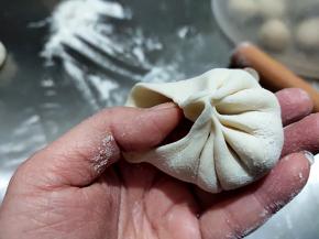 左手将面皮托在手掌中，放适量肉馅，然后右手将面皮边缘捏起，像折纸扇一样，最后封口。