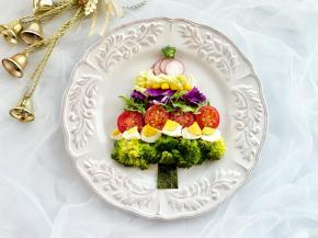 在花环沙拉的顶部中间放一个蝴蝶结。用海苔剪出圣诞树的树干，西兰花摆在最下面一层，然后用各种食材菜一层一层的摆出圣诞树的三角造型，顶部放一片秋葵即可。