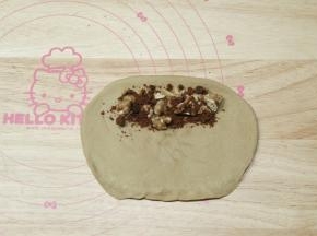 翻面，横向放置，整理成长方形，底部按扁。面团顶部放上一长条核桃碎和一大勺红糖。