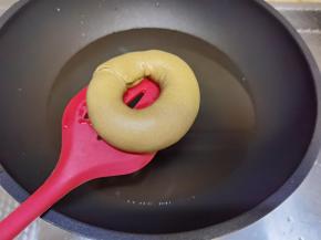 糖和水倒入不粘锅中，大火微微煮沸，转最小火（不要完全煮沸，烤出的贝果会皱皮）。取出发酵好的贝果面团，烤箱立刻转200度开始预热。提起油纸和贝果，倒扣入糖水中煮30秒，煮的时候将油纸拿掉即可！然后翻面再煮30秒，捞出略微抖掉水分后放在烤盘上。