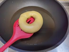 糖和水倒入不粘锅中，大火微微煮沸，转最小火（不要完全煮沸，烤出的贝果会皱皮）。取出发酵好的贝果面团，烤箱立刻转200度开始预热。提起油纸和贝果，倒扣入糖水中煮30秒，煮的时候将油纸拿掉即可！然后翻面再煮30秒，捞出略微抖掉水分后放在烤盘上。