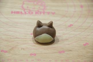 2份面团用保鲜膜包好，松弛20分钟。先做1号柴犬。将35克可可面团用手（千万不要带手套，徒手）搓成椭圆形，底宽头圆。4克白色面团搓圆后按扁成三角形，贴合在可可面团下半部分，形成柴犬的脸，一定要贴紧。3克可可面团分成2半，捏成三角形耳朵，安装在头部即可！