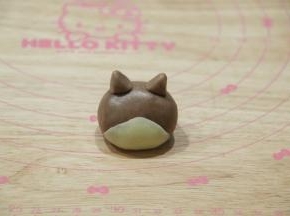 2份面团用保鲜膜包好，松弛20分钟。先做1号柴犬。将35克可可面团用手（千万不要带手套，徒手）搓成椭圆形，底宽头圆。4克白色面团搓圆后按扁成三角形，贴合在可可面团下半部分，形成柴犬的脸，一定要贴紧。3克可可面团分成2半，捏成三角形耳朵，安装在头部即可！