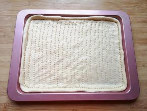 擀成一张和烤盘大小一致的面饼，放进烤盘里，用叉子扎满小孔，防止饼皮在烤制的过程中中间凸起。 