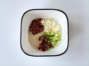 碗中加入一勺辣椒面、一勺蒜末、一勺白芝麻、一勺葱花、一勺切碎的小米椒（我用的是干辣椒）。