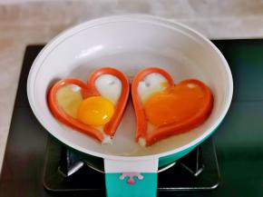 锅中刷上少许油，将火腿肠做出爱心形状，小火加热，磕入鸡蛋。