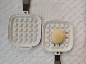 在一面华夫饼盘上放上包好馅料的面胚。略微按扁。