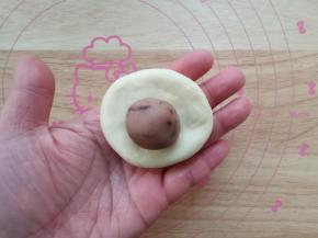 把豆沙分成12克一个，搓圆。取一个松弛好的面团，按扁成中间厚两边薄，翻面放上馅料球。