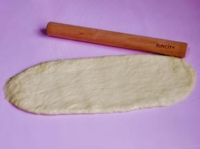 取一块松弛好的面团，用擀面杖擀长舌状，由上往下卷起来。