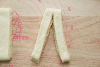 小心的略微擀宽。然后横向切成7条。取一条，从中间切开，顶端不切断。