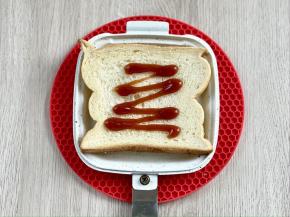 在三明治烤盘中放一片吐司，挤上番茄酱。