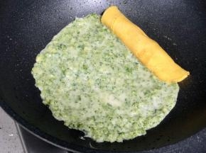 把蛋黄卷放在平底锅的一边，然后倒入蛋清和西兰花碎的混合液，摊平。
