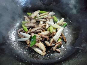 接着倒入香菇煸炒一两分钟，然后加入青蒜白色部分，翻炒至青蒜断生。