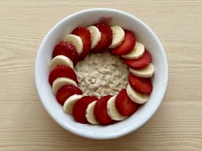 把煮好的燕麦粥倒入碗中，一片草莓和一片香蕉交错沿着碗边摆好一圈；