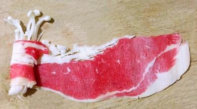 冷冻的肥牛片微微解冻后取一片展平取适量金针菇放在肥牛片一侧顺一个方向紧紧的卷起