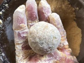 再抓一把玉米面粉在手心，裹满菜团子，边捏边裹，至看不见菜