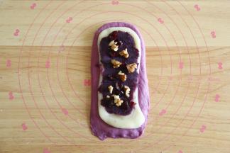 取一擀开成长方形，翻面后放上扯开成差不多形状的麻薯，放上紫薯泥，熟核桃碎和蔓越莓。