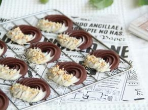 冷凉好的曲奇，一边蘸上适量白巧克力，撒上榛子仁碎，喜欢果干或者蔓越莓的小伙伴，可以加一些蔓越莓碎。