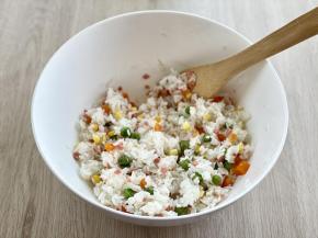 把煮熟的豌豆、玉米粒、胡萝卜丁和火腿碎一起倒入米饭中，搅拌均匀。