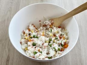把煮熟的豌豆、玉米粒、胡萝卜丁和火腿碎一起倒入米饭中，搅拌均匀。