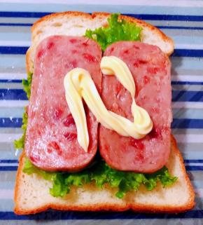 保鲜膜平铺在底部摆上一片吐司放上生菜再摆上午餐肉淋上沙拉酱