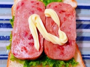 保鲜膜平铺在底部摆上一片吐司放上生菜再摆上午餐肉淋上沙拉酱