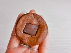 取一块面团，放上巧克力片包起来，揉圆再压扁。