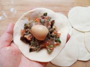 取一个包子皮，放上豆角肉馅，再放上一个卤好的鹌鹑蛋。