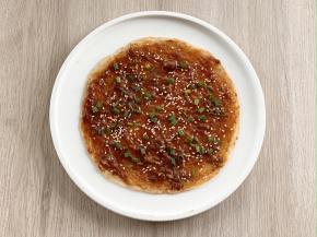 在手抓饼上抹上酱料，撒上葱花和熟白芝麻