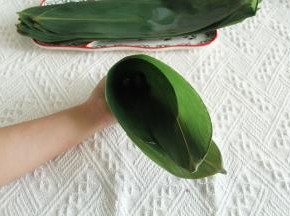 粽叶两张反向叠起，比较毛的两面贴合，宽的部位在两头。右边1/3处往里折成漏斗型。