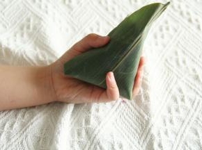 右手把突出那部分粽叶贴着馅料，盖住馅料。左右两边往下压紧。