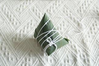 顶部多出的部分粽叶，往一边折过去贴合就好，一个手指压住线，一圈一圈把粽子裹住就可以啦！