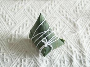 顶部多出的部分粽叶，往一边折过去贴合就好，一个手指压住线，一圈一圈把粽子裹住就可以啦！